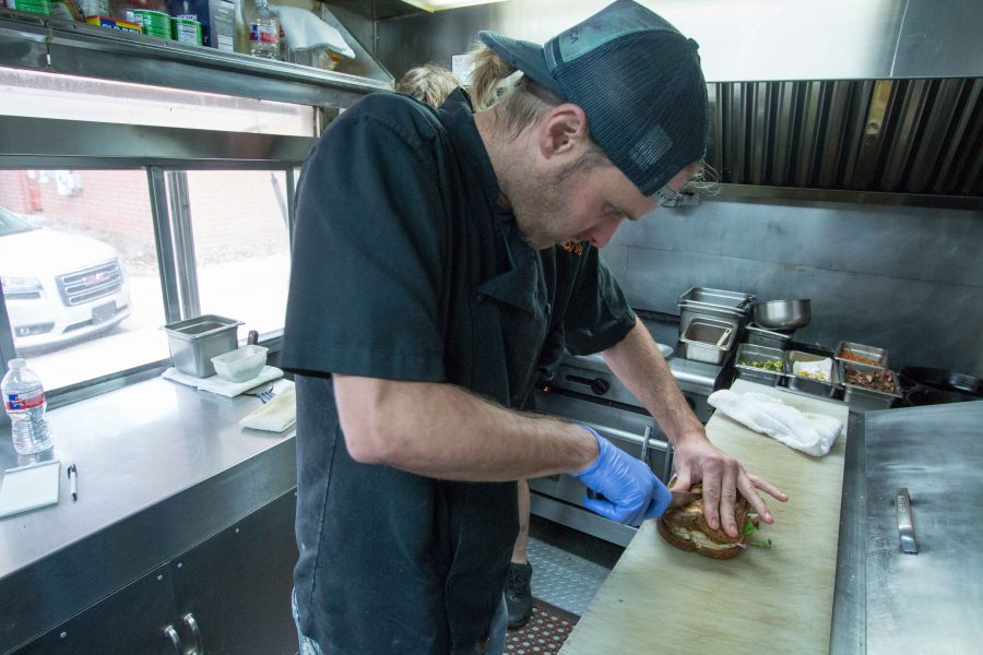 The Flying Stoves chef Rob Schauf cuts the fall chicken sandwich in half, on Nov. 23. The sandwich has roasted chicken, pickled red onions, seared cheese and other tasty ingredients.