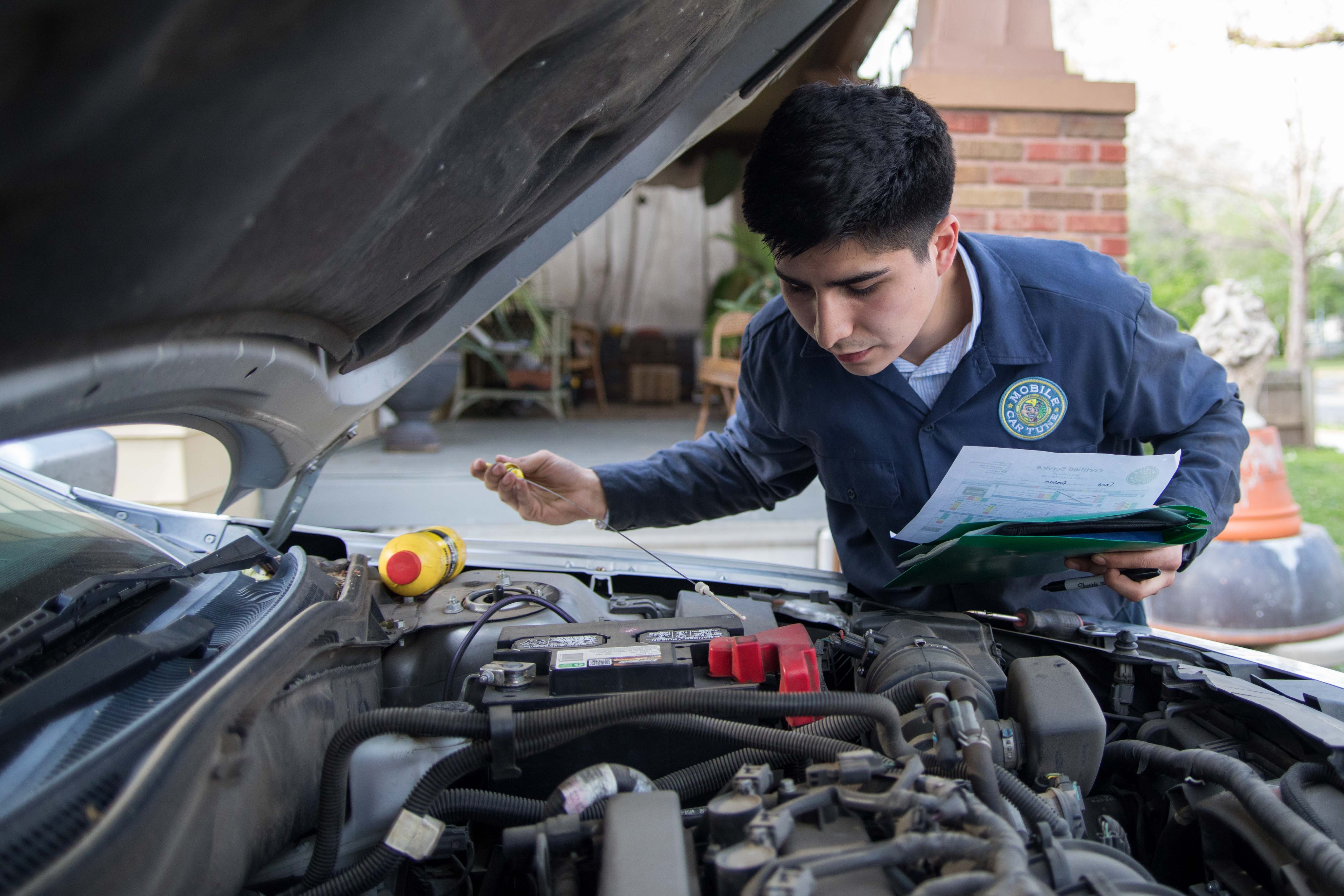 Ernie Cisneros checks the transmission fluid for his client Dan Edwards on Wednesday evening. Cisneros owns a business called Mobile Car Tune that performs car maintenance services at people's homes.
