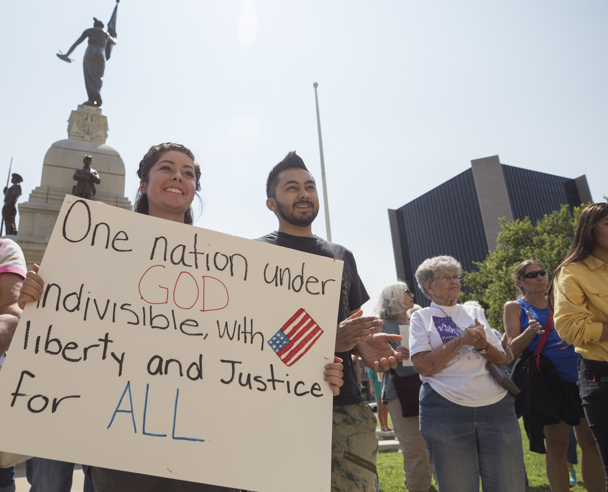 Wichita State Students Karen Segura and Jaime Segura hold up a sign and applaud during the #HereToStay support event held at the Historical County Courthouse on Tuesday afternoon. (Sept. 5, 2017)