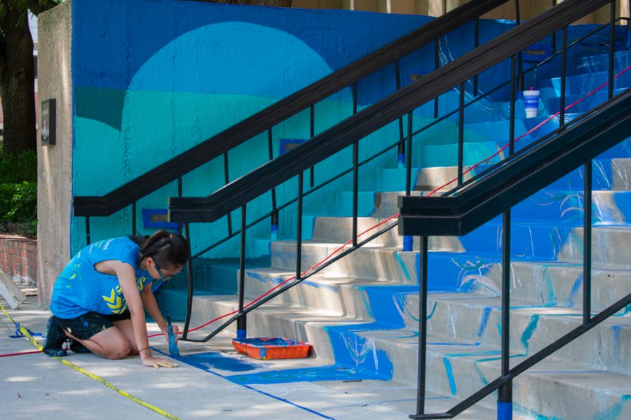 Sarah Myose, a senior honors baccalaureate student studying art and sociology, applies mixed paints to their work on the south side of Clinton Hall. The piece will be done for the start of the fall semester.