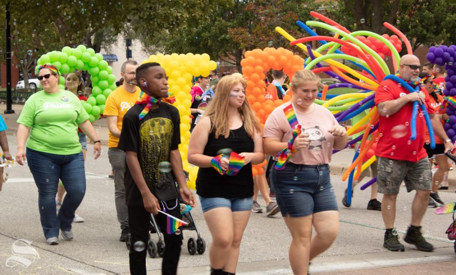 Three students walk through the 2019 Wichita Pride Parade. Behind them, rainbow-colored balloons spell SPIRIT.