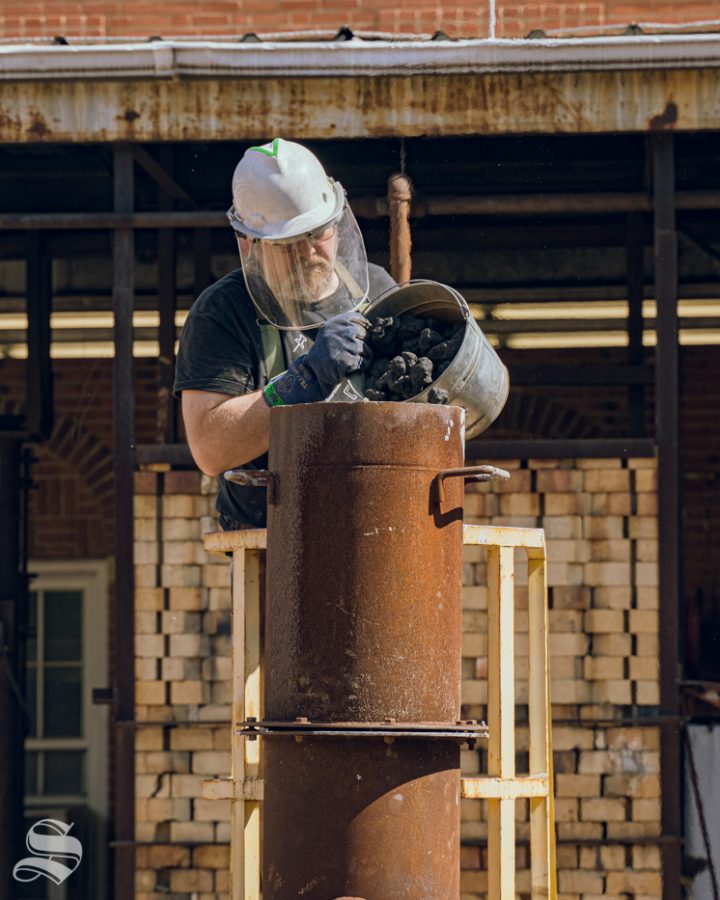 Barry Badgett pours coal into a cupola furnace. Iron Pour was hosted by the sculpture guild on Oct. 5 at Henrion Hall.