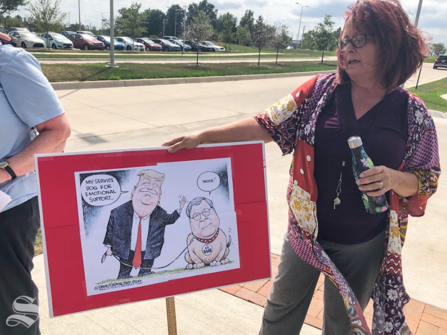 A protester displays a sign with a cartoonish depiction of President Donald Trump and Attorney General William Barr on Oct. 2 at the Law Enforcement Training Center. There was a roundtable event held in the training center which Barr attended.