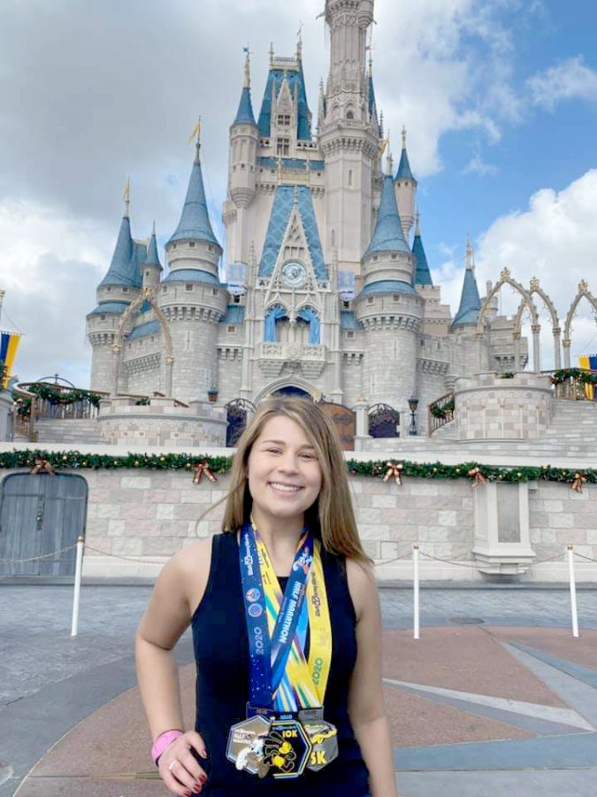 Madeline Shonka stands in front of the castle at Disney World with her medals from running a 5k, 10k, and half marathon for three consecutive days.