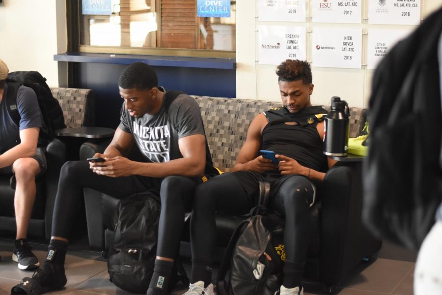 Wichita State junior Trey Wade and freshman Tyson Etienne sit on their phones at Texas Wesleyan University, reacting to the news of the cancellation of the AAC conference championship tournament.