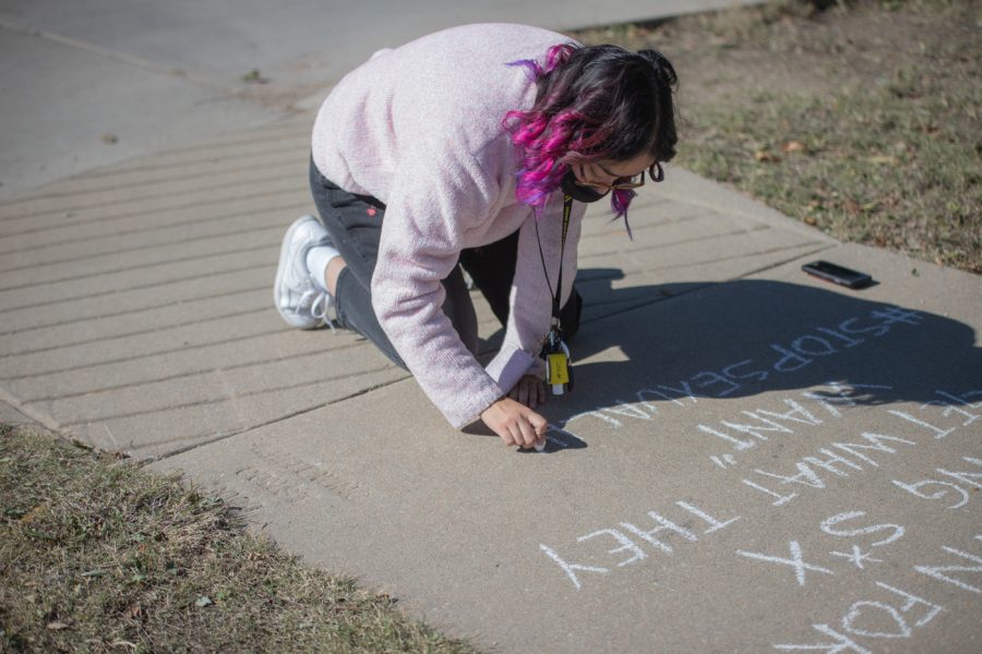 Alondra Aguilera writes with chalk outside of the presidental inaguration on Oct. 29 at the Metroplex. Aguilera was one of the many protesters to hold signs. She decided to help make an impact and spread the word as she wrote quotes to fight discrimination and attached the hashtag #STOPSEXUALHARASSMENT.