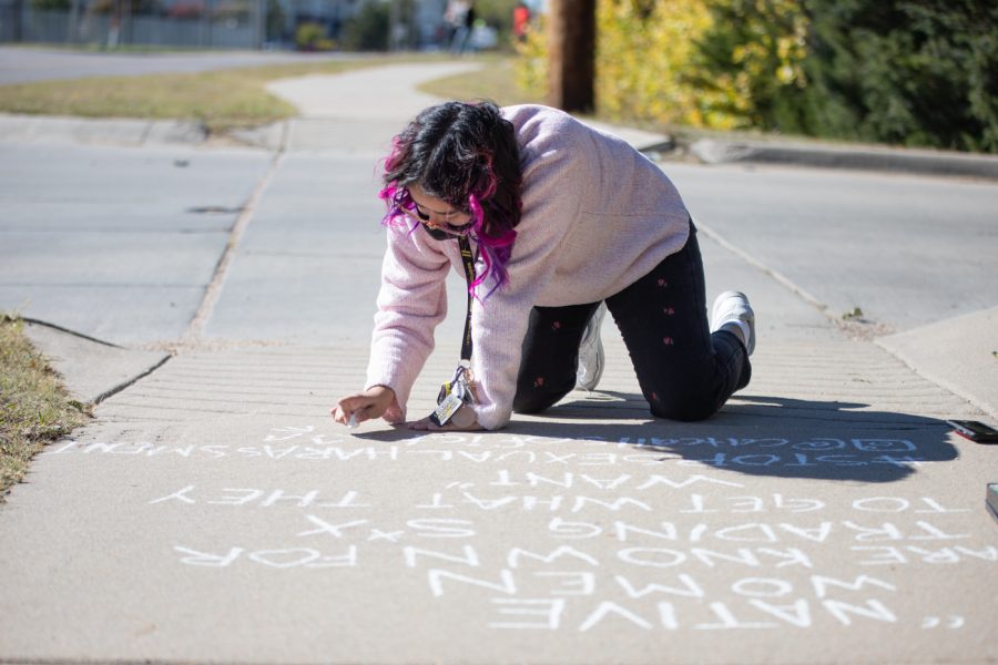 Alondra Aguilera writes with chalk outside of the presidental inaguration on Oct. 29 at the Metroplex. Aguilera was one of the many protesters to hold signs. She decided to help make an impact and spread the word as she wrote quotes to fight discrimination and attached the hashtag #STOPSEXUALHARASSMENT.