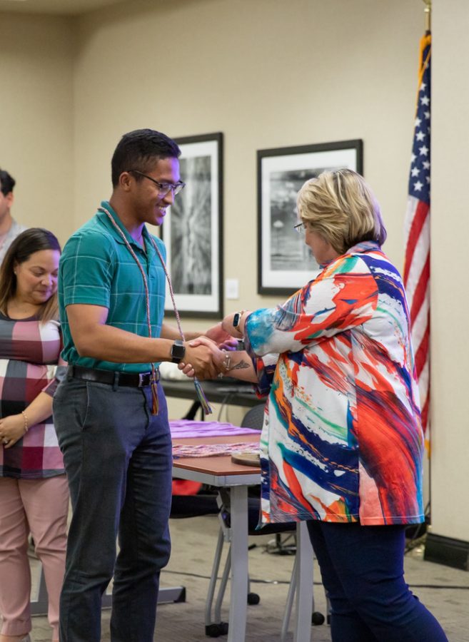 Graduate Anthony Mai receives a challenge coin from Vice President for Student Affairs Teri Hall after receiving a Spectrum cord.