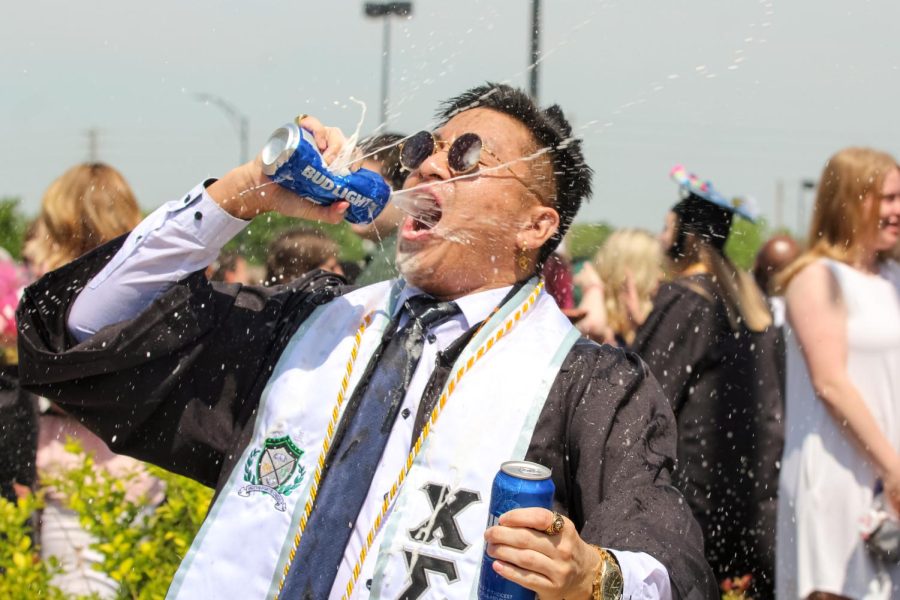 Spring 2022 graduate celebrates by smashing two Bud Light cans together and drinks them after the Spring Commencement Ceremony on May 14.