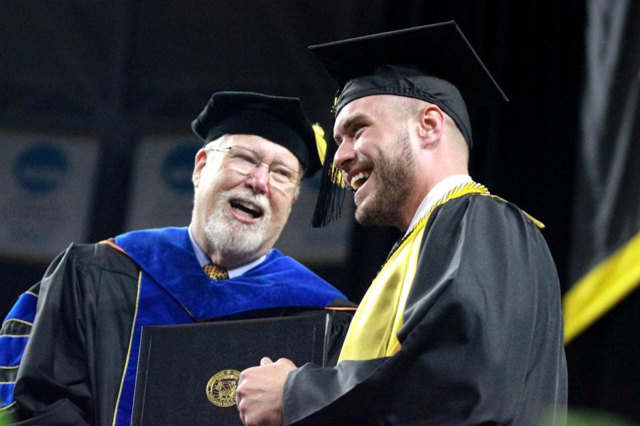 Graduate poses with his diploma on stage at the Charles Koch Arena on May 14.