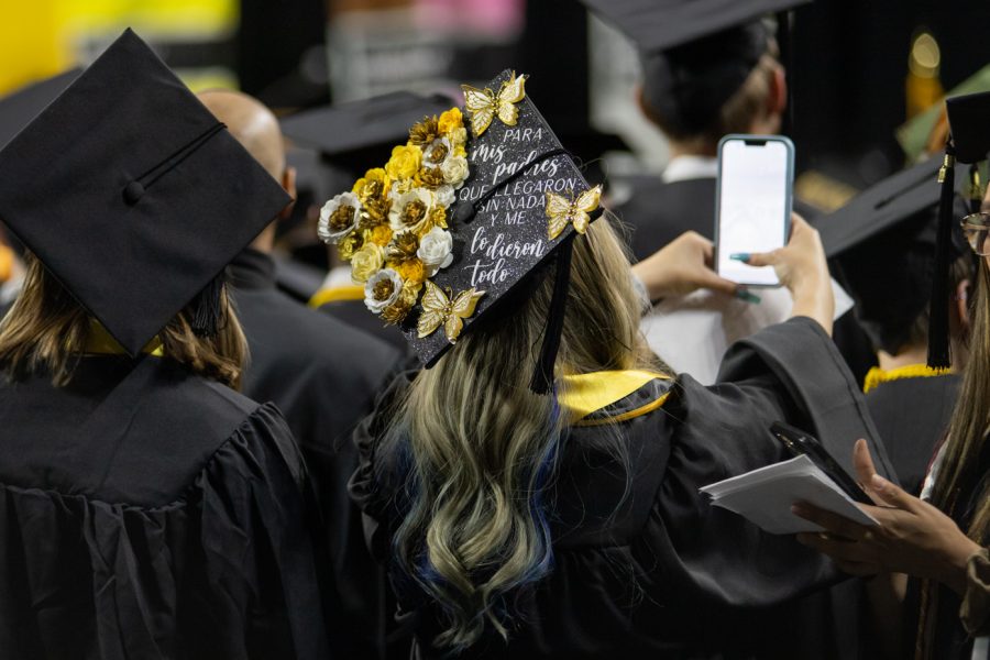 With a decorated cap, a graduate student takes a video of Koch Arena before the ceremony begins