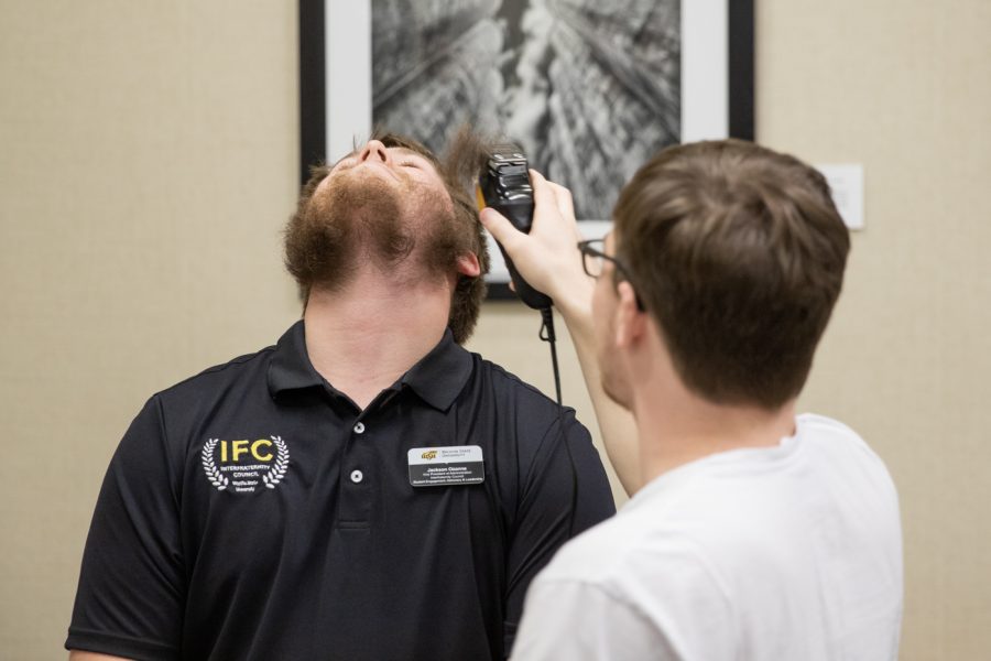 Jackson Ozanne, vice president of administration with the Interfraternity Council, tilts his head back while Logan Hutchens, computer science major,  shaves some of his beard off.