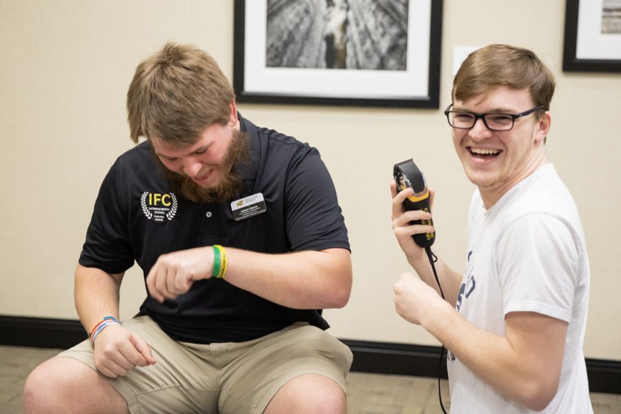 Jackson Ozanne, vice president of administration with the Interfraternity Council, spits beard out of his mouth after Logan Hutchens, computer science major,  shaves some of it off.