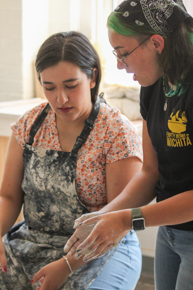 A Wichita State Ceramic Guild member guides a community member on how to shape their bowl at the Ulrich Build-A-Bowl event. 