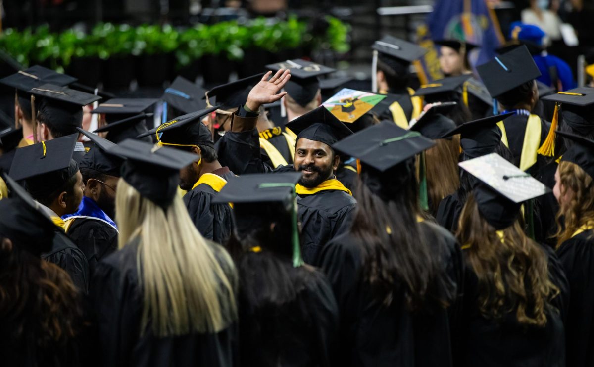 A fall 2023 graduate waves to family and friends in the audience of Charles Koch Arena. 