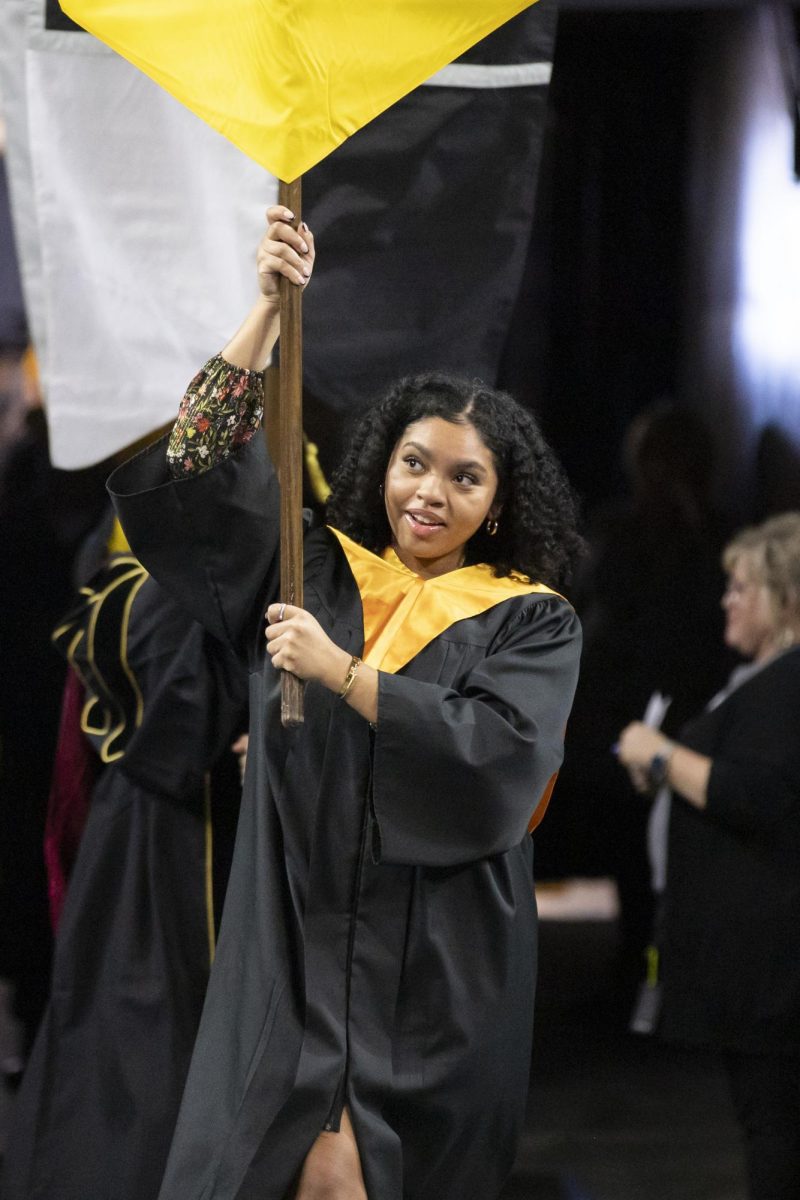 Student Body President Iris Okere walks into the Fall 2023 Commencement, holding a Wichita State University banner on Dec. 17, 2023.