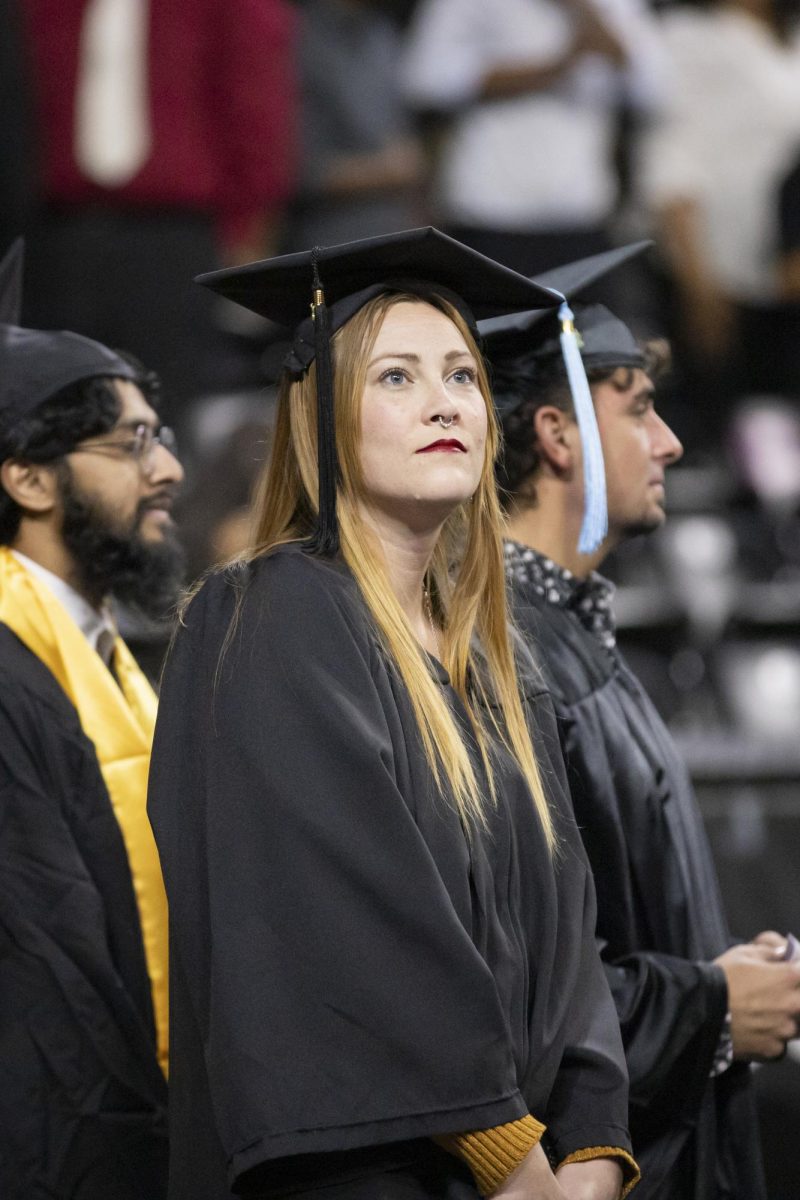 A fall 2023 graduate looks up into the crowd at Charles Koch Arena as graduates walk into the room for commencement on Dec. 17.