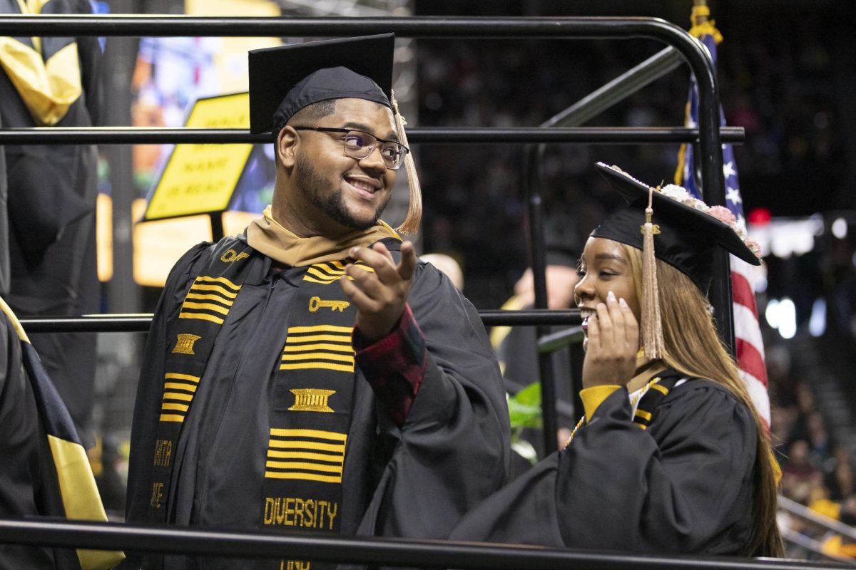 Fall 2023 graduates laugh and talk together as graduates walk up to the stage to receive diplomas on Dec. 17. The 126th Commencement took place inside Charles Koch Arena.