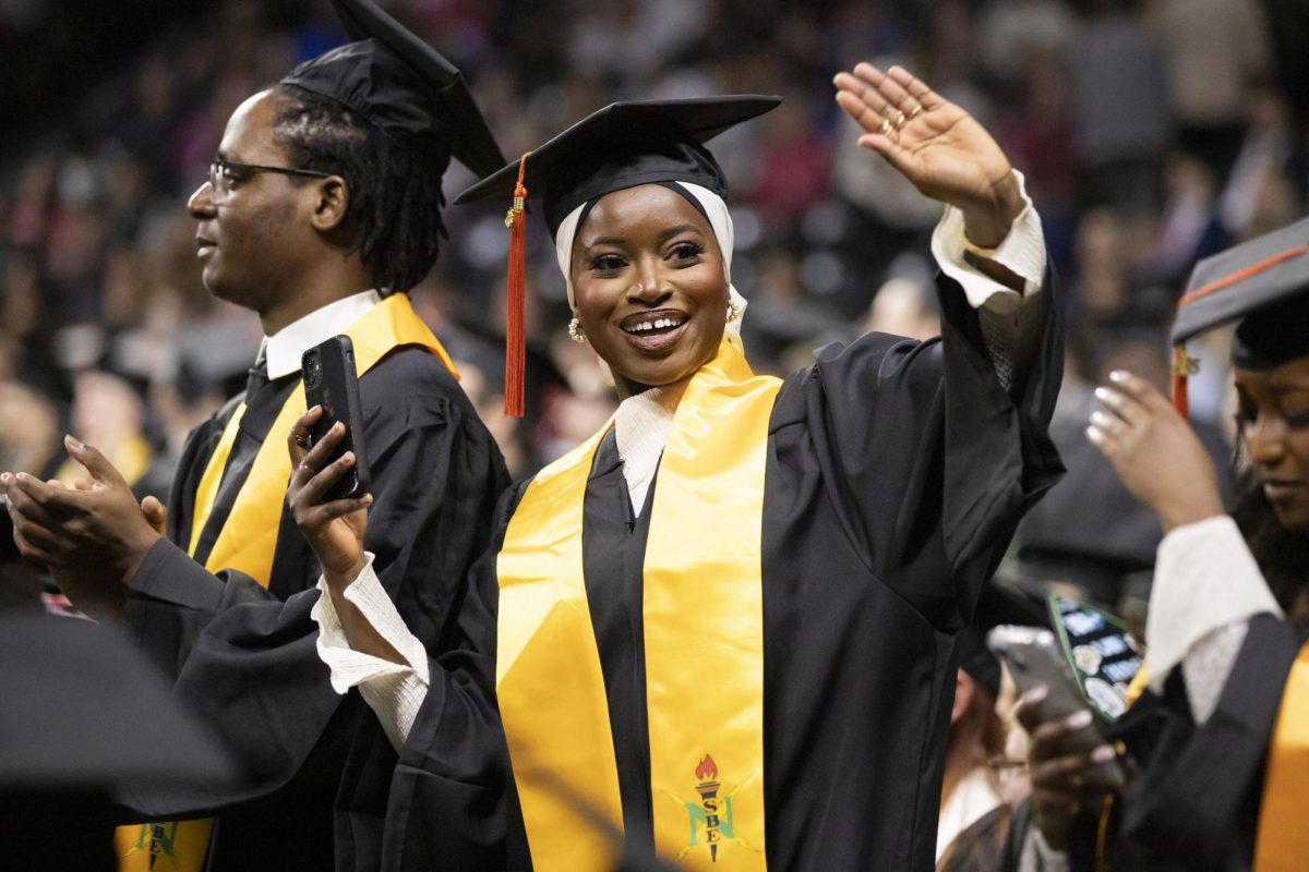 A fall 2023 graduate waves to family and friends in the audience of Charles Koch Arena. 