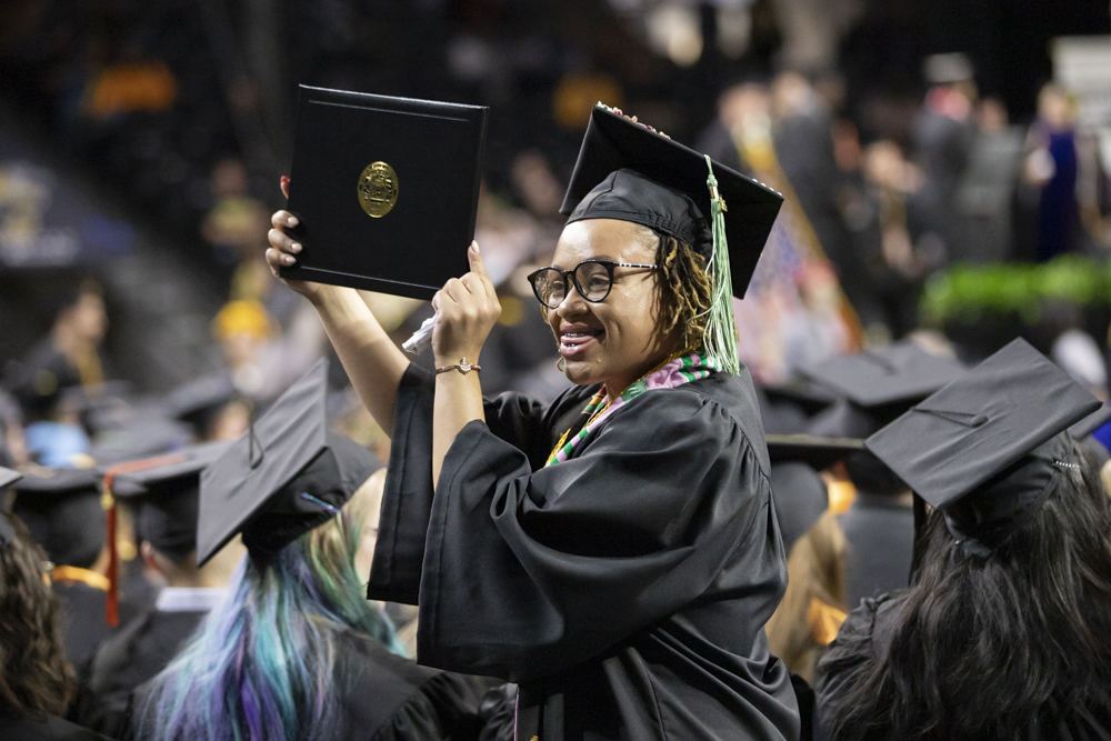 After walking the stage, a fall 2023 graduate holds up her diploma to family and friends in Charles Koch Arena on Dec. 17.
