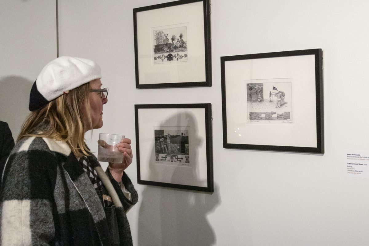 An audience member enjoys a drink while viewing Marco Hernandezs gallery showing Sin Perder A Mis Raíces (Without Losing My Roots) of his prints at the Wichita Art Museum.