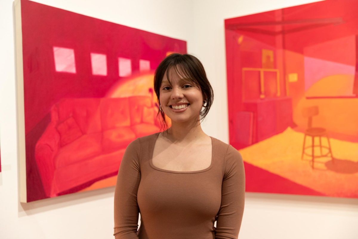 Recent+Wichita+State+graduate+Paola+Iseley+poses+in+front+of+her+artwork+at+the+capstone+exhibition+reception+in+the+Clayton+Staples+Gallery.+Iseley+graduated+in+May+and+is+pursuing+a+future+art+career.