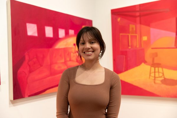 Recent Wichita State graduate Paola Iseley poses in front of her artwork at the capstone exhibition reception in the Clayton Staples Gallery. Iseley graduated in May and is pursuing a future art career.