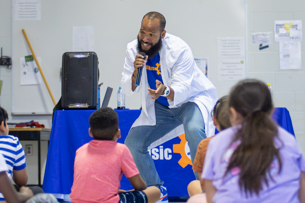 After donning a lab coat, Roy Moye III explains the science behind a baking soda and vinegear reaction. Moye had the Linwood Elementary students participate in several experiments to show that STEM is about asking questions and trying to explain outcomes.