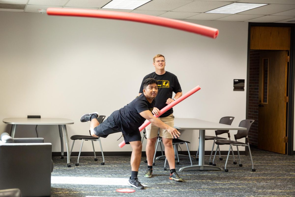 Richard Mai launches a pool noodle across the bottom floor of Ablah Library during the inaugural Faculty/Staff Olympics while teammate Matthew Screnock watches. Mai and Screnock are both advisers in the Barton School of Business.