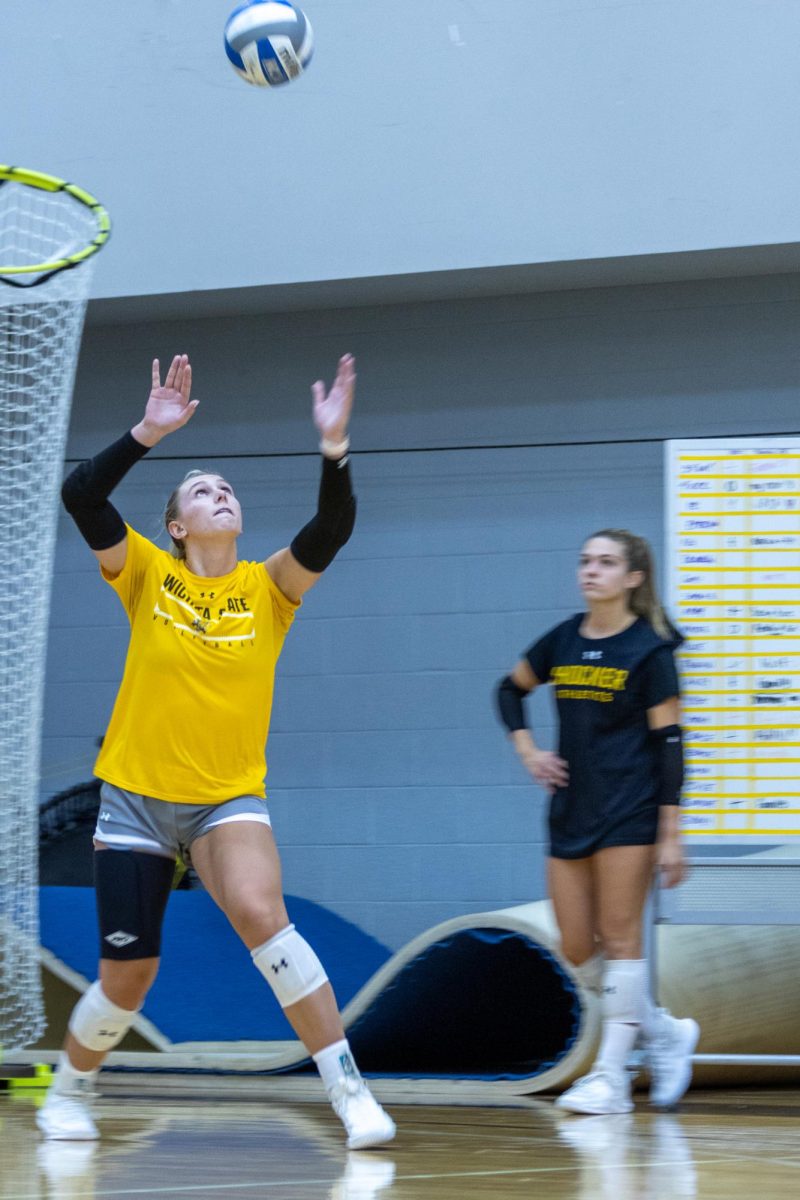 Junior outside hitter Brooklyn Leggett serves to the opposing side as senior Annalie Heliste watches from the sideline during a team practice scrimmage on Aug. 15.