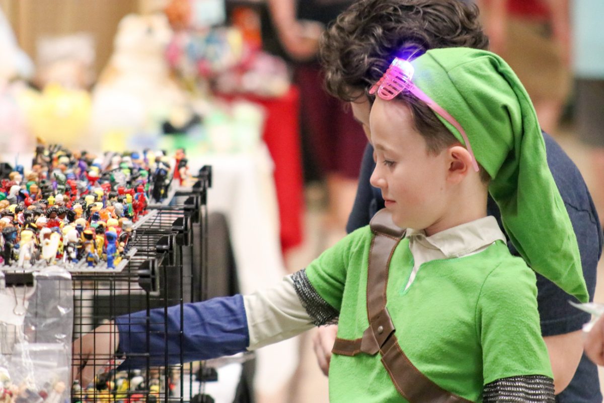 A boy cosplaying as Link from "The Legend of Zelda" video game series examines all of the custom LEGO mini-figures at a booth. Many children stopped by to look at the custom LEGO Mini-figures due to their visual appeal.