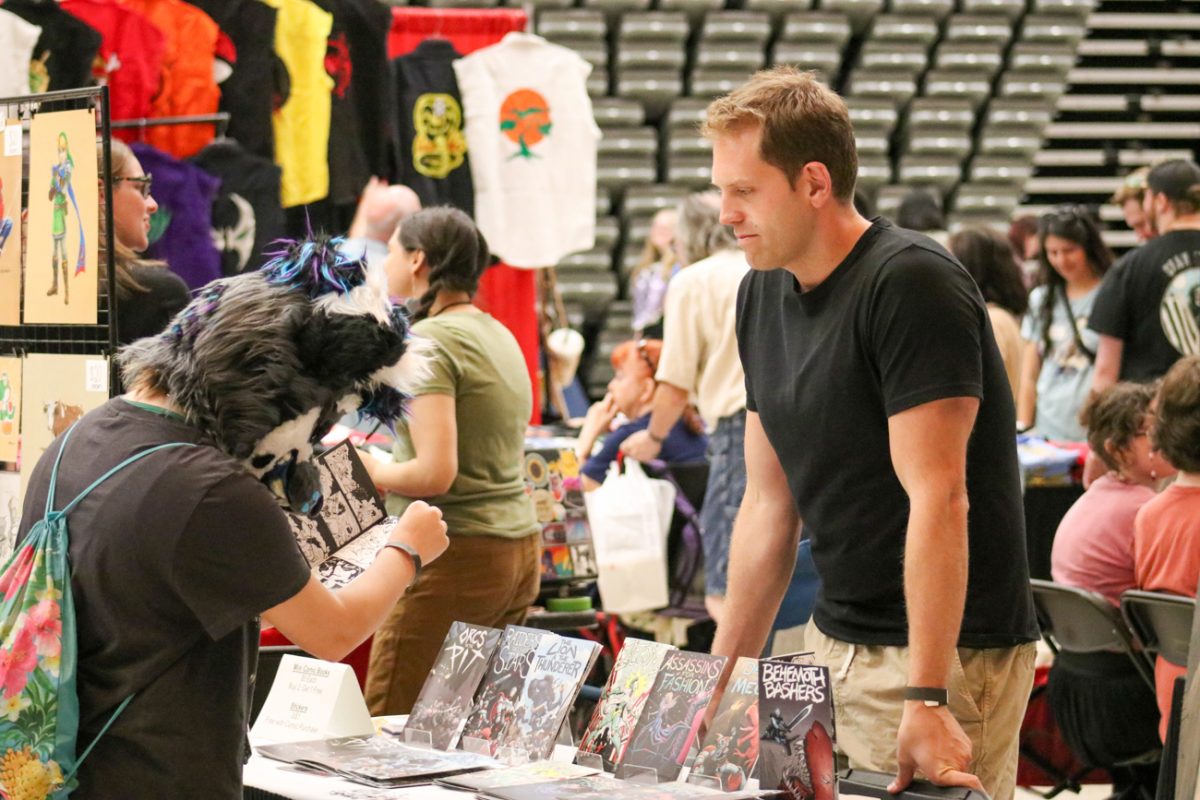 An ICT Comic Con attendee examined Colton Strathman's original comic, "Behemoth Bashers", as Strathman himself watched. 