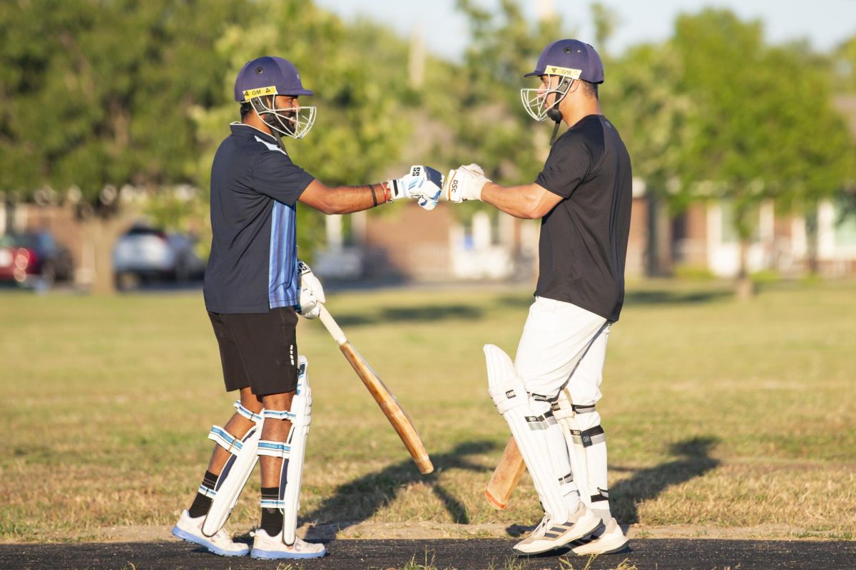 Sai Charan Reddy and Kamran Hafeez hit their bats together and fistbump after switching positions in a game of cricket on Sept. 27. WSU's Cricket Club practices at Dr. Glen Dey Park weekly.