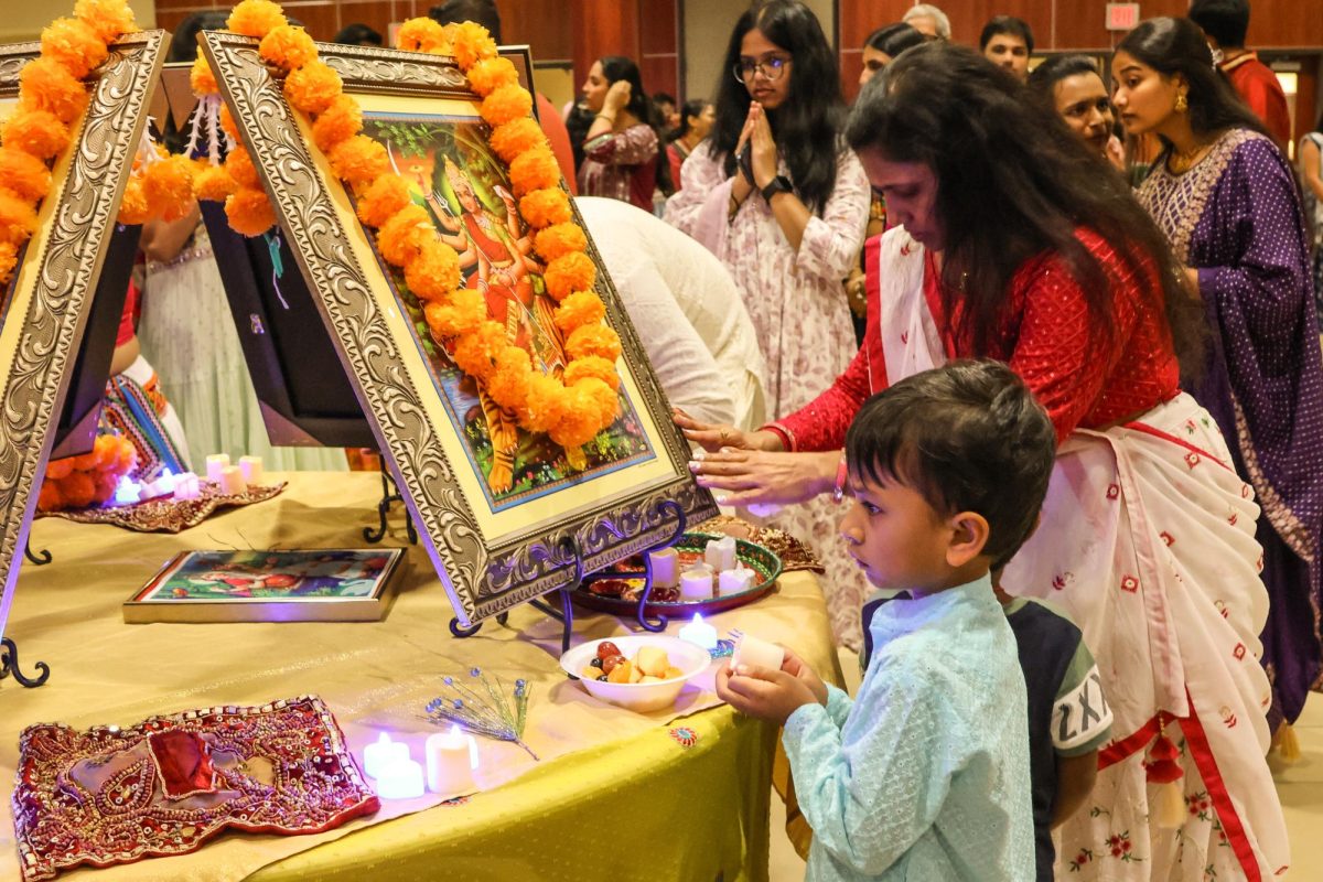 A community member seeks blessings from the goddess Durga, while a child holds candles in front of the goddess. Touching the goddess's photo and presenting offerings is a way of expressing devotion.