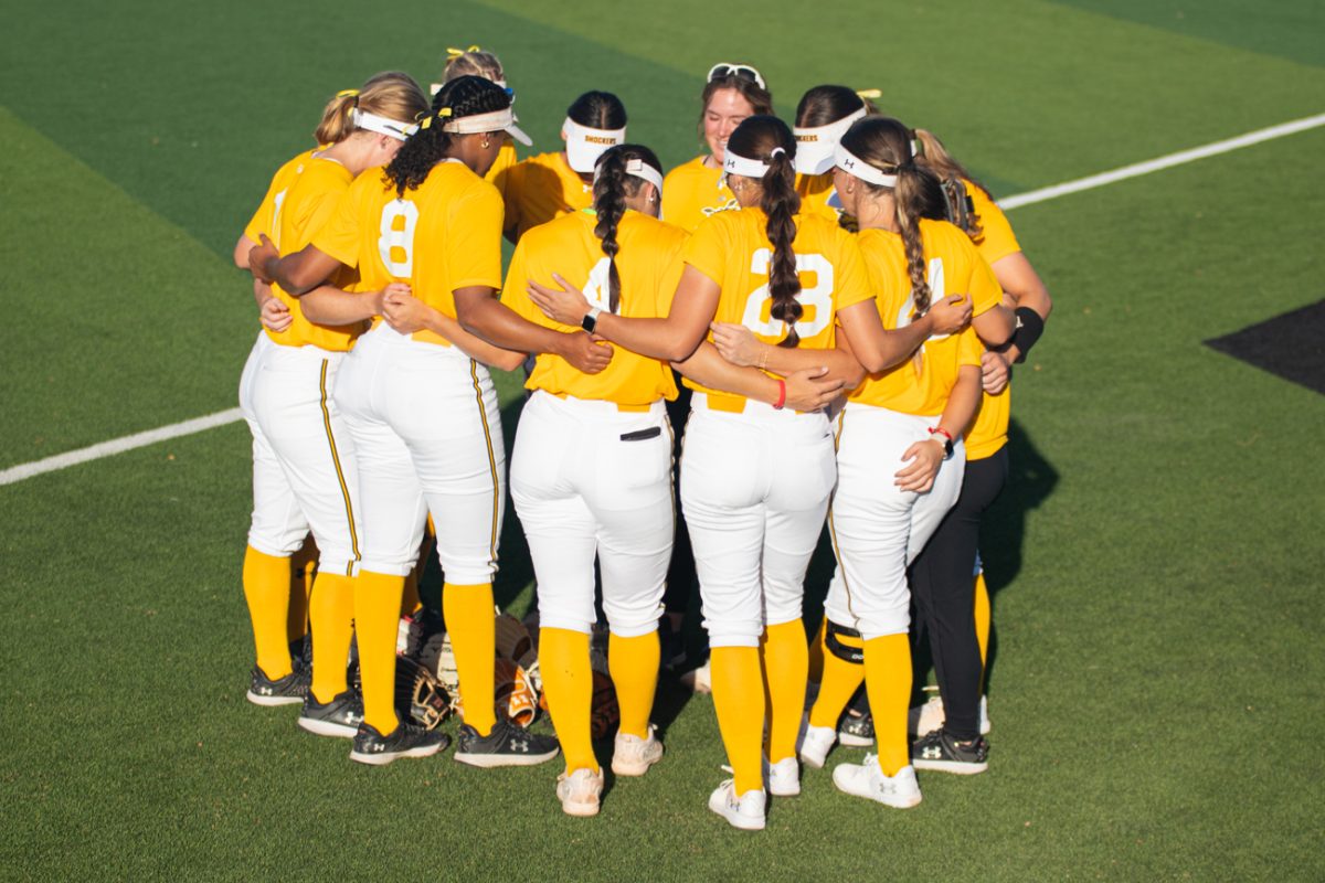 Softball players huddle up before the exhibition match against Butler Community College on Oct. 3. The game was played In Wilkins Stadium and was free to all students with ID.