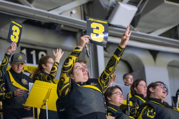 Jocelyn Mallonee, a piccolo flute player, holds up a sign after Wichita State's men's basketball team scored a 3-pointer. Mallonee is a member of the Shocker Sound Machine and has been performing at WSU home basketball games since 2021.