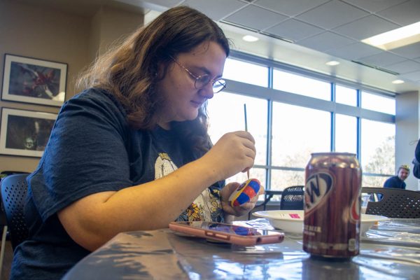 An attendee of the Geology Club's pet rock painting event outlines the hat of Pomni, a character from "The Amazing Digital Circus."