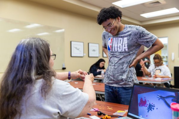 Beadworker Michelle Conine helps Araylius Coronado tie off his spiral stitch bracelet during the beadworking class on May 1. The event was one of four collaborative beadworking sessions hosted by the Indigenous Student Collective and the Office of Student Engagement &amp; Belonging.