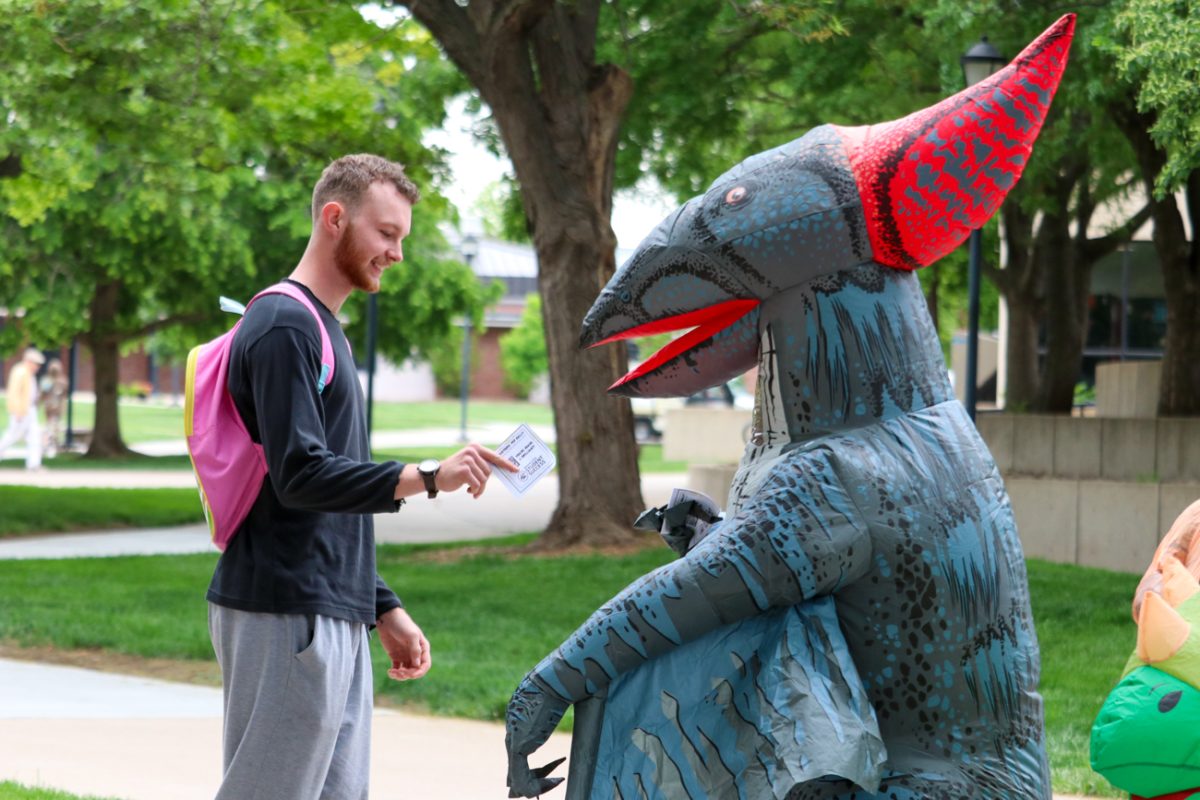 Raven Garrison, an adviser with OneStop, hands a student a card with affirmations while dressed as a dinosaur. Garrison and other student success staff danced and handed out more than 80 compliment cards to students preparing for finals week.