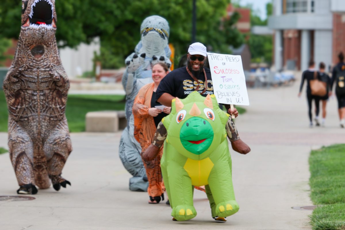 Courtney Lockhart, a member of Student Outreach & Support and CARE TEAM, leads a line of dinosaurs toward the Dorothy and Bill Cohen Honors College and Shocker Hall. The group of dinosaur-dressed support and success staff shared positive messages and words of encouragement during their pop-up Prehistoric Pep Rally on May 6.