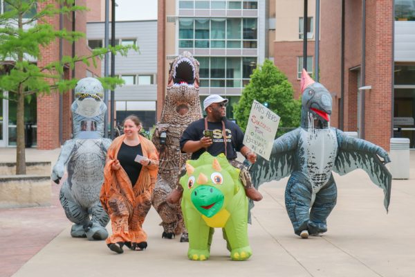 Courtney Lockhart, a member of Student Outreach & Support and CARE TEAM, leads a line of dinosaurs out of Shocker Hall. The group of dinosaur-dressed support staff shared positive messages and words of encouragement during their pop-up Prehistoric Pep Rally on May 6.