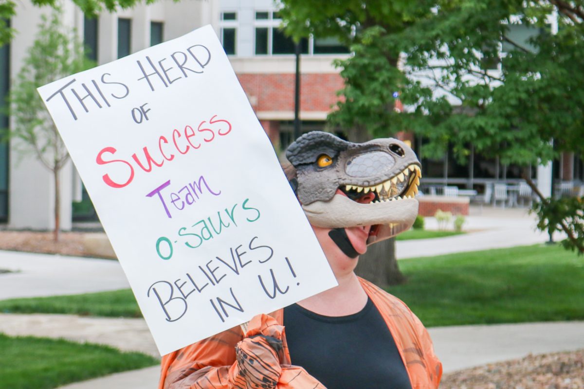 Dressed in a dinosaur mask and wielding a motivational sign, Assessment and User Experience Librarian Sara Rue roars like a dinosaur. Rue's mask made a dinosaur sound when she opened the mouth.