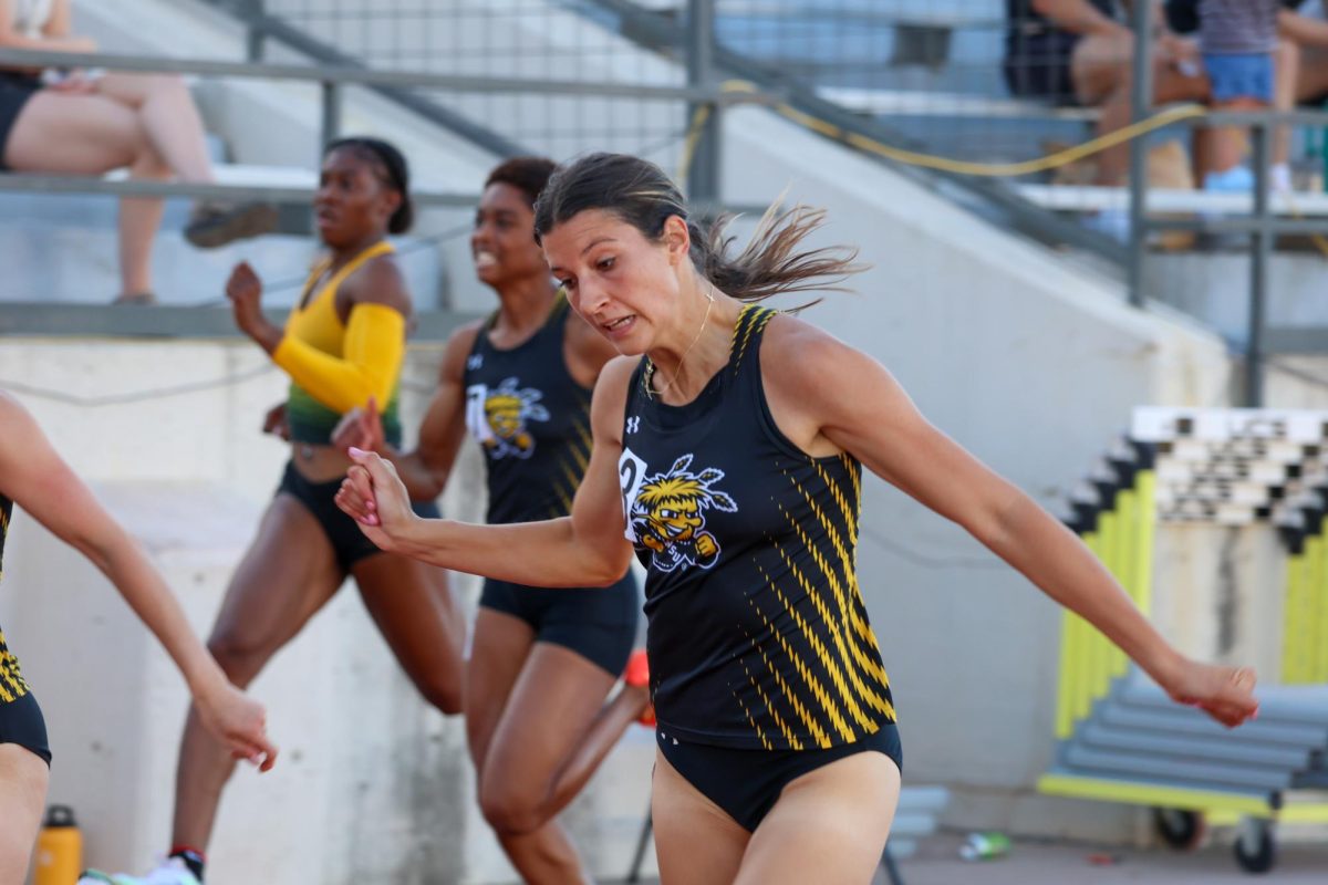 Junior Sadie Millard leans forward as she crosses the finish line of the women's 100-meter on May 9. Millard finished in second at the Shocker Open with a time of 11.85.