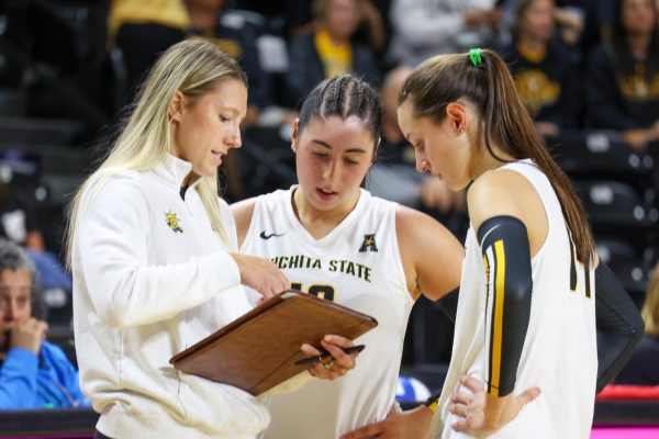 Wichita State volleyball assistant coach Katie Zimmerman talks with juniors Maddie Wilson (14) and Jordan Heatherly (16) before the second set against Arkansas on Sunday, Aug. 31, at Koch Arena in Wichita, Kansas. The Shockers won in five sets, 3-2.