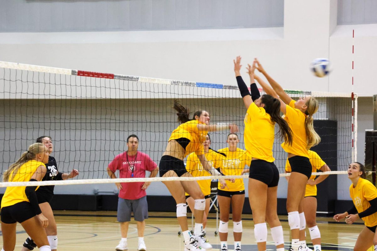 Junior middle blocker Maddie Wilson spikes the ball past two of her teammates at practice on Aug. 4. Wilson made 121 kills last season in 76 sets.
