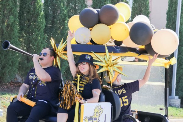 Sarah Beth Estes, dean of the Fairmount College of Liberal Arts and Sciences, rides on the back of a golf cart in the Shocktoberfest parade holding up the Shocker hand sign. 