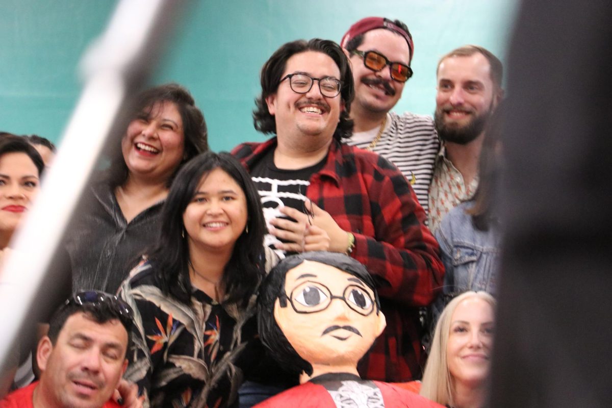 Artist Justin Favela grins as he waves over his friend and photographer Mikayla Whitmore to join in the photo before the timed photo is taken. The group photo commemorated the Family Fiesta on Saturday, Nov. 15.