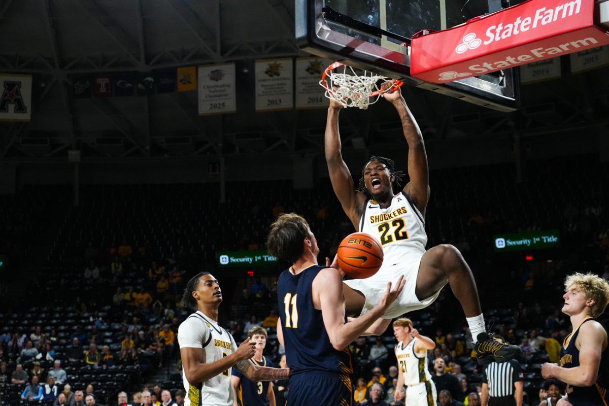Wichita State men's basketball freshman center Noah Hill (22) hangs on the rim after slamming home a dunk against Mount Marty on Dec. 2. The Shockers won 95-69.