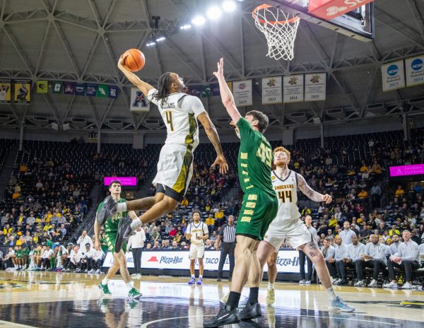 Wichita State men's basketball redshirt freshman forward TJ Williams (4) soars for a dunk over Charlotte's Anton Bonke (49) Feb. 4. Williams ended the game with six rebounds and three assists.