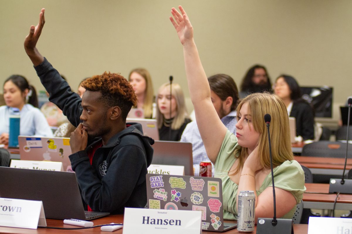 Sen. Emanuyel Brown and Riley Hansen raise their hands during the Student Senate meeting on April 24, 2024. Senators voted on and installed the next session's speaker of the senate and student body treasurer. (File photo) 